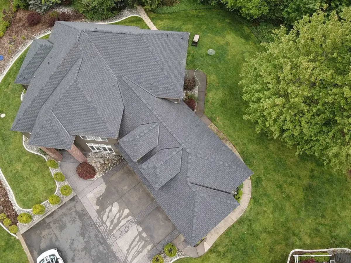 Aerial view of a finished multi-gable gray shingle roof with a manicured lawn